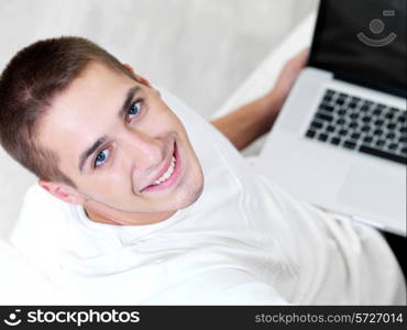 happy young guy using laptop and lying on the sofa - high angle