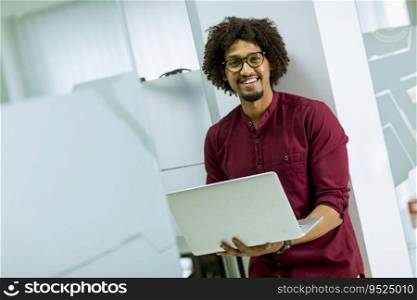 Happy young handsome African American IT specialist wearing glasses working on his laptop in the office