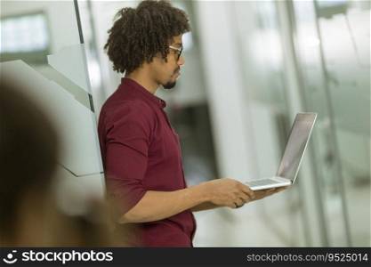 Happy young handsome African American IT specialist wearing glasses working on his laptop in the office