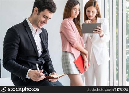 Happy young handsome businessman reading book and working in office with colleagues and friend at workplace. Corporate business people group.