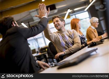 Happy young handsome entrepreneurs in casual clothes at business office giving high fives to each other