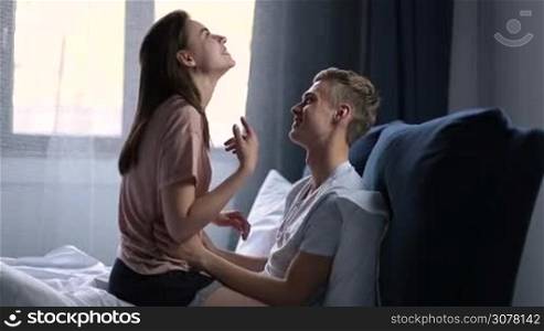 Happy young handsome man and beautiful woman lying in bed and enjoying each other in the morning. Romantic couple in love embracing and kissing while enjoying lovely morning together in bedroom after awakening.