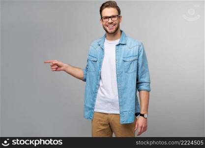 Happy young handsome man in jeans shirt pointing away standing against grey background.. Happy young handsome man in jeans shirt pointing away standing against grey background
