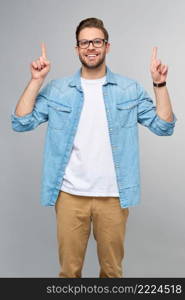 Happy young handsome man in jeans shirt pointing away standing against grey background.. Happy young handsome man in jeans shirt pointing away standing against grey background