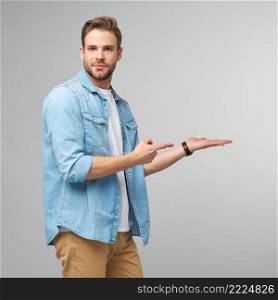 Happy young handsome man in jeans shirt pointing away standing against grey background.. Happy young handsome man in jeans shirt pointing away standing against grey background