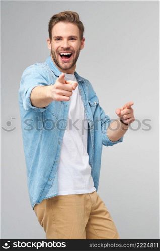 Happy young handsome man in jeans shirt pointing on camera standing against grey background.. Happy young handsome man in jeans shirt pointing on camera standing against grey background