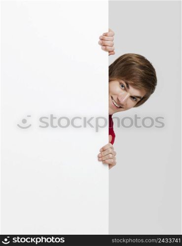 Happy young hiding and looking behind a blank white card