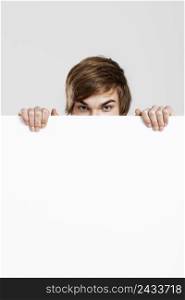 Happy young hiding and peeking behind a blank white card