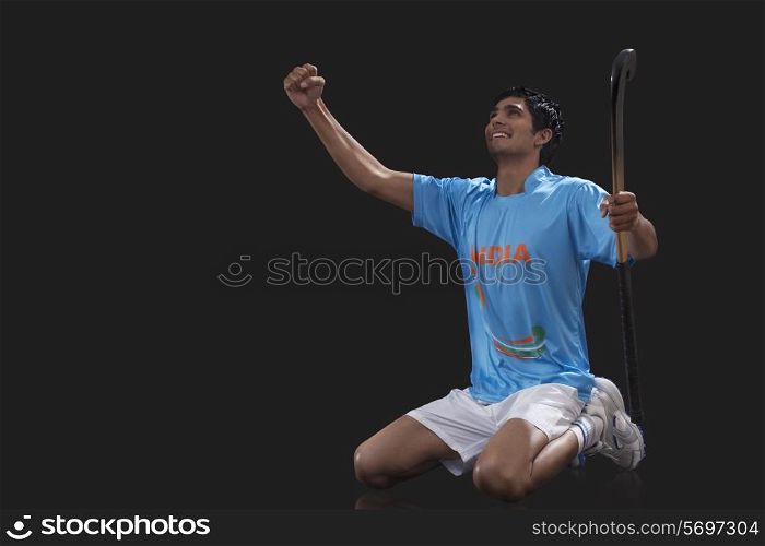 Happy young hockey player with stick celebrating success over black background