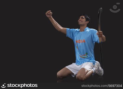 Happy young hockey player with stick celebrating success over black background