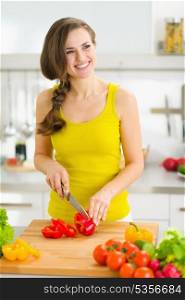 Happy young housewife cutting bell pepper in kitchen