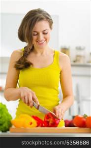 Happy young housewife cutting bell pepper in modern kitchen