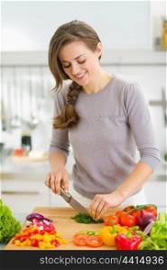 Happy young housewife cutting fresh dill in kitchen