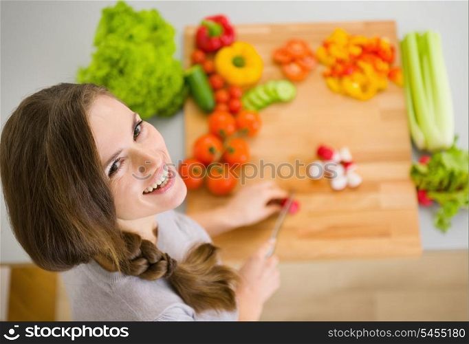 Happy young housewife cutting fresh vegetables