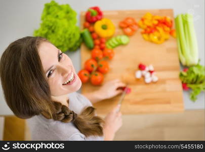 Happy young housewife cutting fresh vegetables