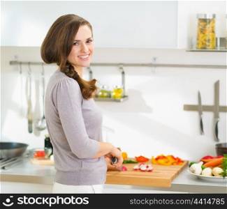 Happy young housewife cutting fresh vegetables in modern kitchen