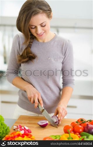 Happy young housewife cutting onion in modern kitchen