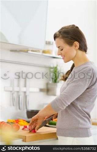 Happy young housewife cutting vegetables on salad in kitchen