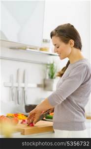 Happy young housewife cutting vegetables on salad in kitchen