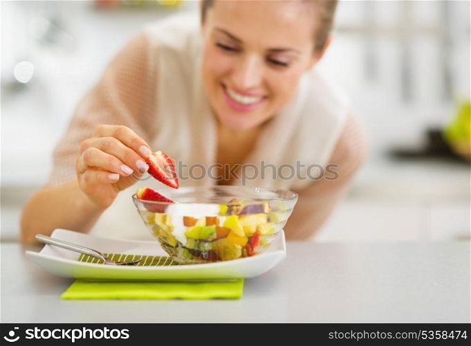 Happy young housewife decorating fruits salad