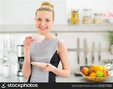 Happy young housewife drinking tea in modern kitchen