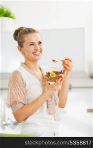 Happy young housewife eating fruits salad