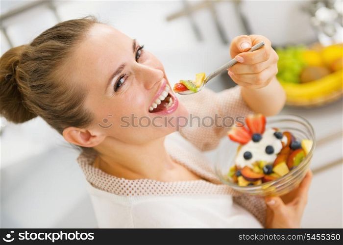Happy young housewife eating fruits salad . rear view