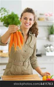 Happy young housewife giving bunch of carrots
