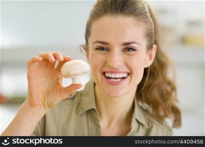 Happy young housewife holding mushroom in kitchen