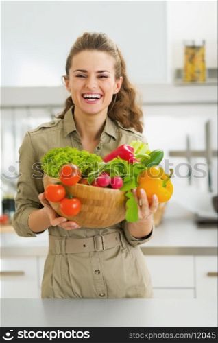 Happy young housewife holding plate full of vegetables in modern kitchen