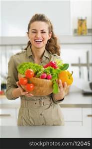 Happy young housewife holding plate full of vegetables in modern kitchen