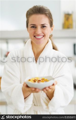 Happy young housewife in bathrobe showing healthy breakfast
