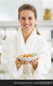 Happy young housewife in bathrobe showing healthy breakfast