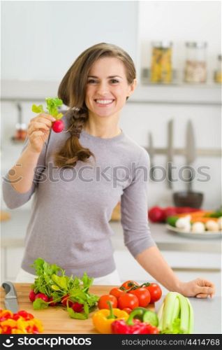 Happy young housewife in modern kitchen showing radish