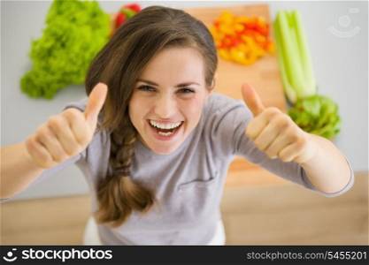 Happy young housewife in modern kitchen showing thumbs up