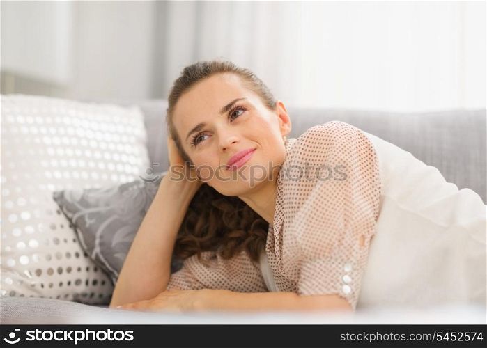 Happy young housewife laying on sofa in living room