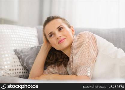 Happy young housewife laying on sofa in living room