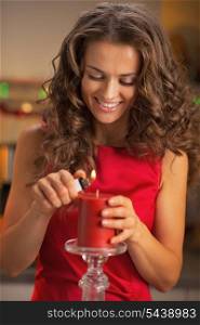 Happy young housewife lighting candle in christmas decorated kitchen