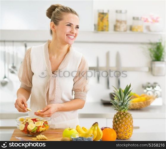 Happy young housewife making fruits salad
