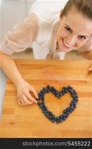 Happy young housewife making heart with blueberries