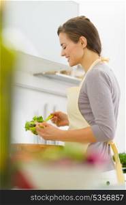 Happy young housewife mixing salad in modern kitchen