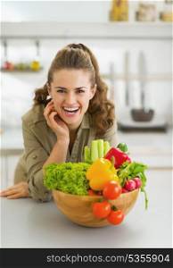 Happy young housewife near plate full of vegetables in modern kitchen
