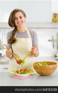 Happy young housewife served plate with fresh vegetable salad in kitchen