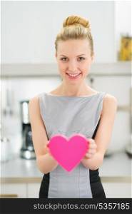 Happy young housewife showing decorative heart in kitchen