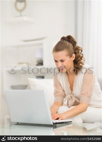 Happy young housewife sitting on divan and using laptop