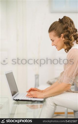 Happy young housewife sitting on divan in living room and using laptop