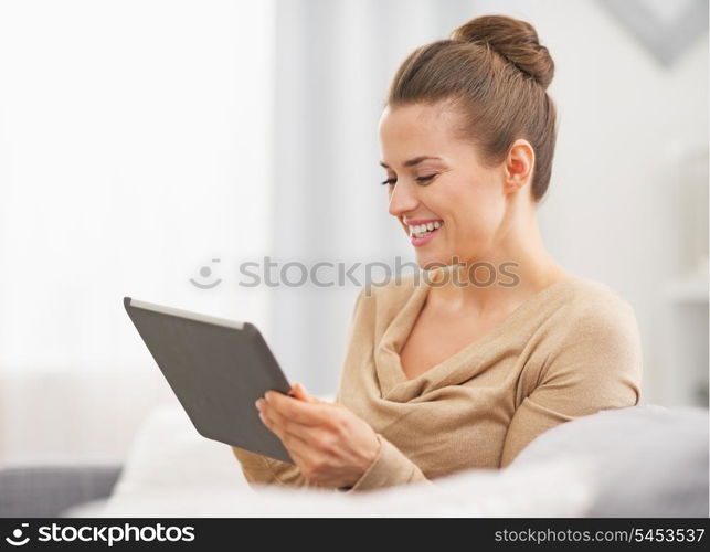 Happy young housewife sitting on sofa and using tablet pc