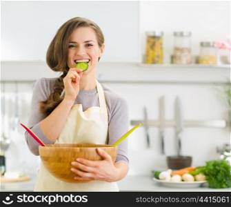 Happy young housewife tasting slice of cucumber from vegetable salad