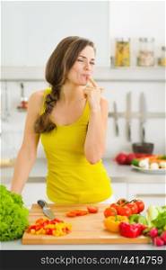 Happy young housewife tasting vegetables while cutting