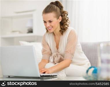 Happy young housewife using laptop in living room
